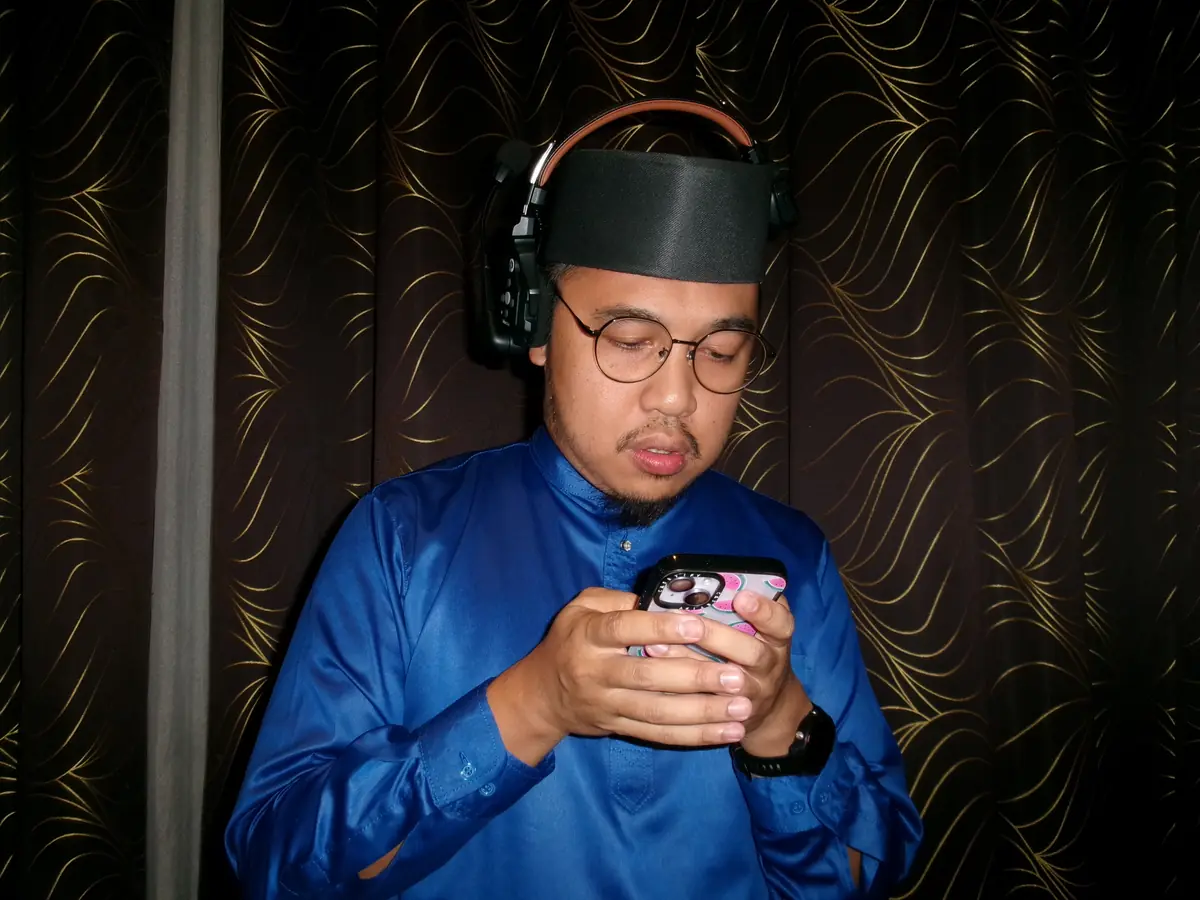Agendas Brunei crew member in blue baju melayu and headset checking the schedule on his phone