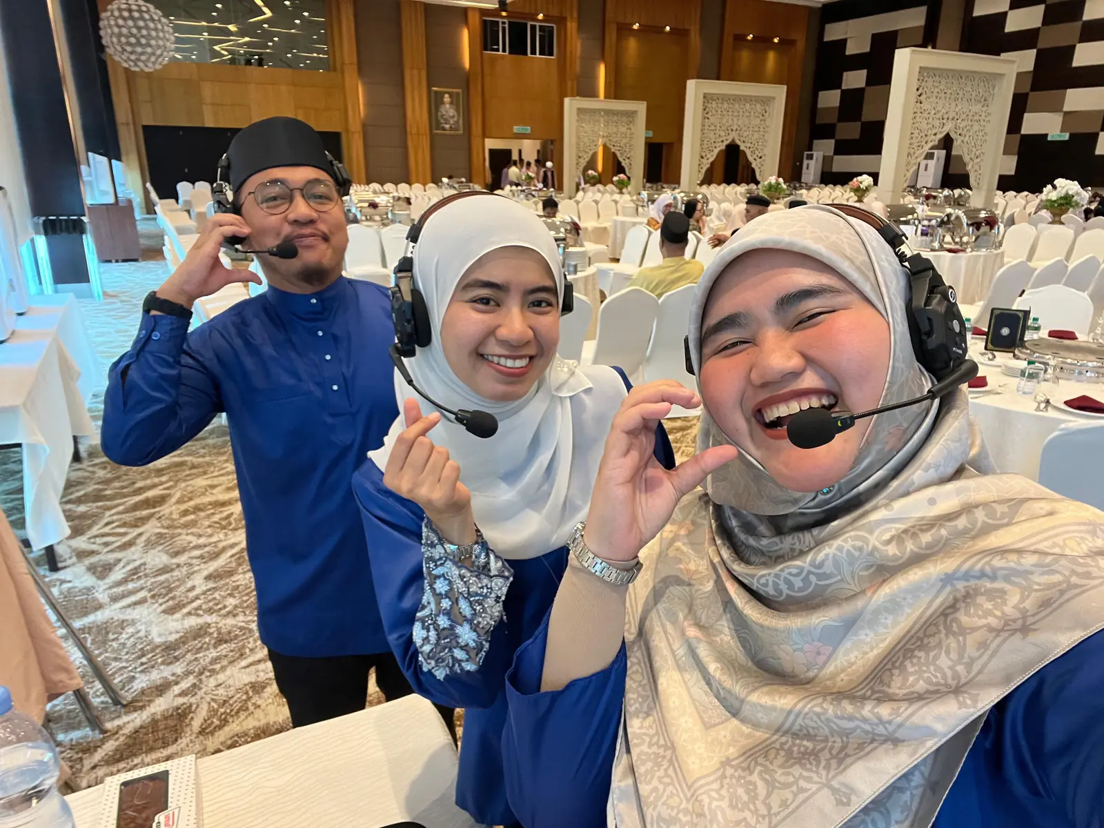 Three Agendas Brunei crew members wearing comms headsets, smiling, in a bright banquet hall